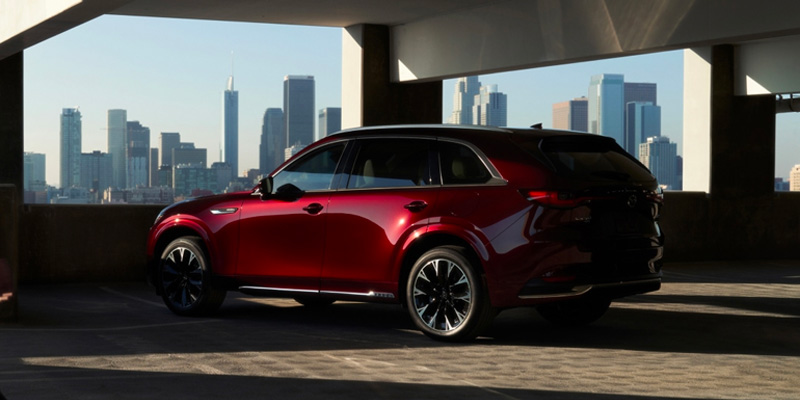 A shiny red Mazda CX-90 parked in a garage, with a city skyline in the background.