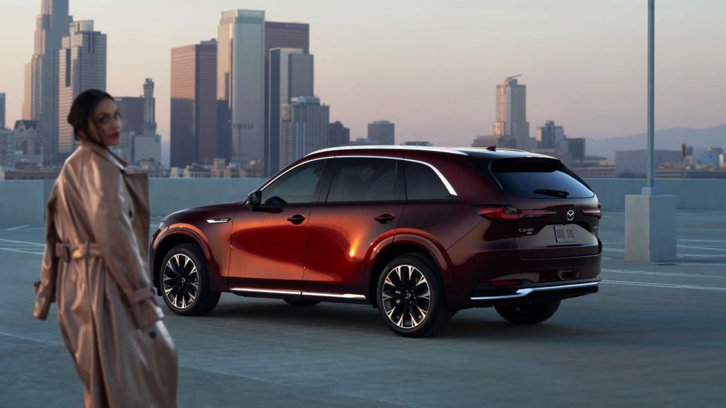 Red Mazda CX-90 parked on a rooftop with a city skyline.