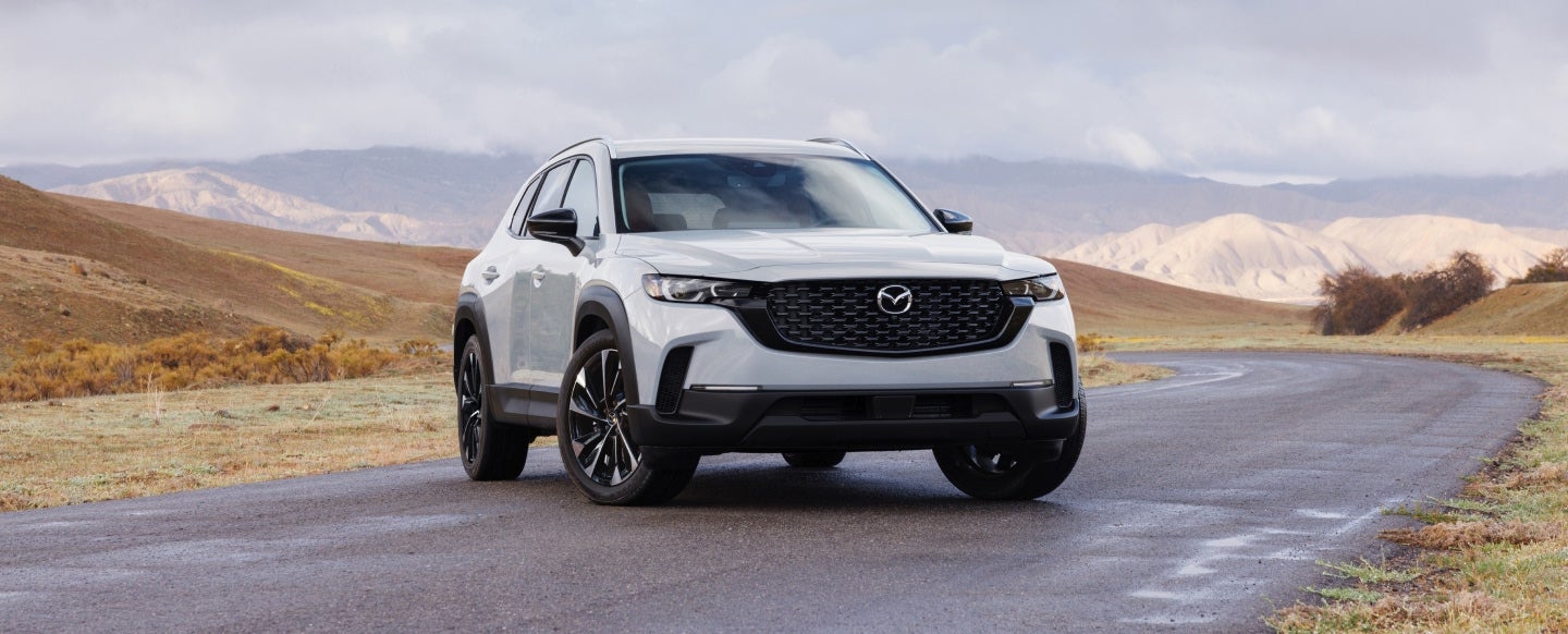 White Mazda SUV parked on a scenic mountain road with rolling hills in the background.